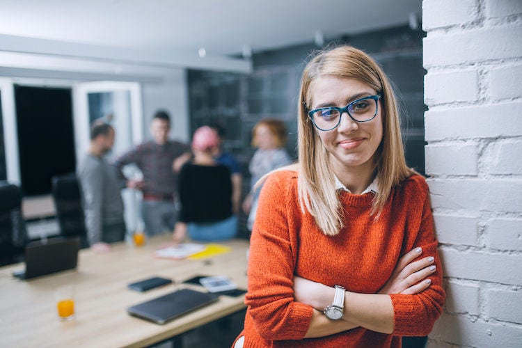 Photo of young business woman in a conference room, with a group of coworkers in backside