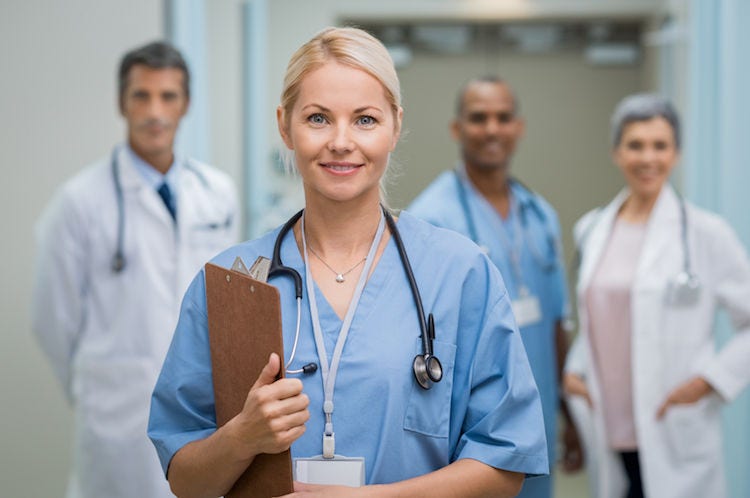 Portrait of a smiling young nurse holding clipboard at hospital. Satisfied female nurse outside operation theatre holding clipboard. Proud female doctor in scrubs looking at camera.