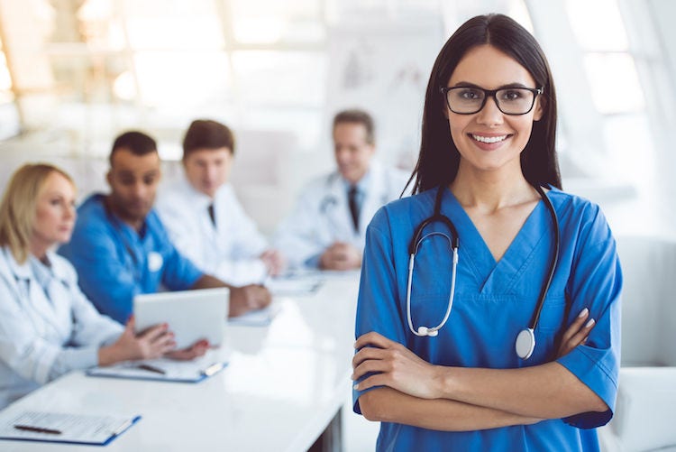 Beautiful young female medical doctor is looking at camera and smiling while her colleagues are sitting in the background