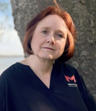 Kathryn Funk wearing a Maryville University v-neck shirt standing in front of a tree